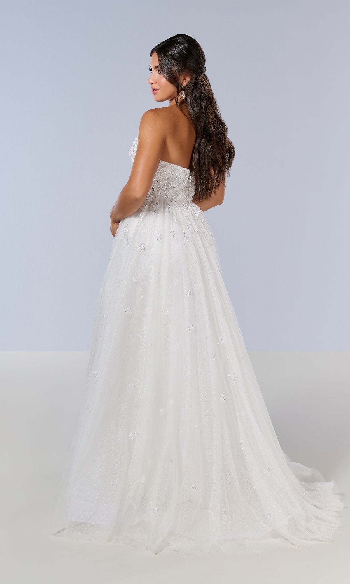 A woman with long dark hair wears the Long Prom Dress: Tiffany 16209, a strapless white gown with a sweetheart neckline, tulle skirt, and subtle embellishments, standing against a plain light background.